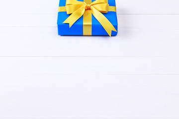 Gift box with yellow bow. Present wrapped with ribbon. Christmas or birthday blue package. On white wooden table.
