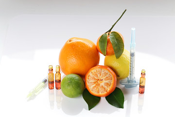 Vitamin C in ampoules, two syringes, mandarin, lemon,  orange and lime on a light background. ...