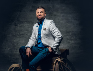 Obraz premium A man dressed in a white jacket and bow tie sits on a wooden.