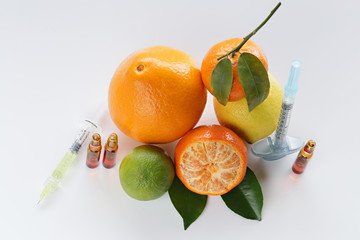 Vitamin C in ampoules, two syringes, mandarin, lemon,  orange and lime on a light background....