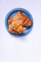 Fresh croissants. Delicious buttered roll in blue plate. French cuisine. On white wooden rustic background.