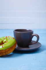 Donuts with cup. Sweet glazed pistachio green donut. Dessert with sprinkles. On blue wooden rustic background.
