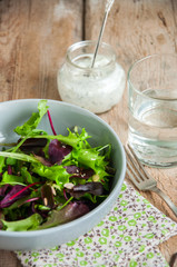 Spring herbs salad with sesame and flax seeds and spicy sour cream sauce on a wooden background. Copy space and close up.