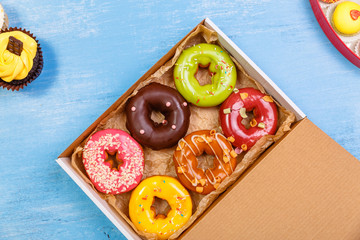 Glazed donuts, cupcakes and macaroons. Sweet dessert in delivery box. Cakes with buttercream. Almond macaron cookies.