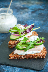 Rye bread with seeds crostiniwith chicken ham  spring herbs red onion and spicy sour cream sauce served on a black stone board.
