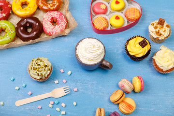 Cupcakes, macaroons and donuts. Mug with whipped cream. Almond macaron cookies with marshmallows. Sweet dessert.