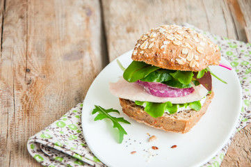 Sandwich with salad herbs chicken ham red onion seeds and spicy sour cream sauce served on a white plate. Wooden background.