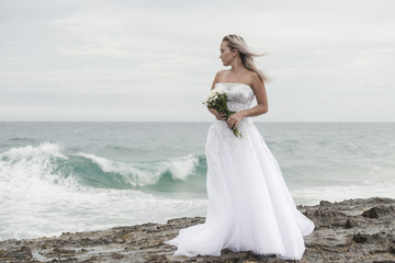 Fototapeta na wymiar Beautiful bride at the beach with a flower bouquet.