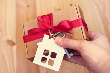 congratulation with the housewarming party/ Holiday gift with the symbols of the house and key, in hand on a wooden background