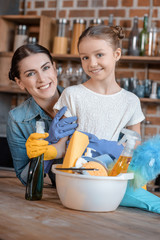 portrait of happy mother and daughter in rubber gloves with cleaning supplies