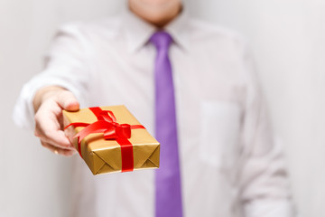Male hand holding a gift box. Present wrapped with ribbon and bow. Christmas or birthday package. Man in white shirt and necktie.