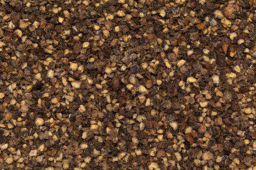 Dried Organic and cracked Black peppercorns (Piper nigrum). Macro closeup background texture. Top view.