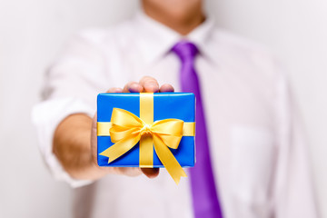 Male hand holding a gift box. Present wrapped with ribbon and bow. Christmas or birthday blue package. Man in white shirt and necktie.