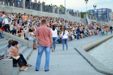 A large gathering of people. Back men on the background of people. People on the promenade waiting for the concert