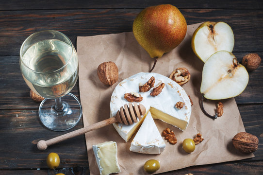 Camembert cheese with walnuts, honey and pears on rustic table. Glass of white wine