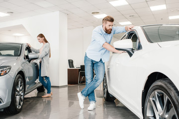 Couple choosing car, man and woman looking on various cars in dealership salon