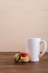 Macaroon cakes. Mockup white tea or coffee cup. Almond sweet cookies. Wooden rustic board.