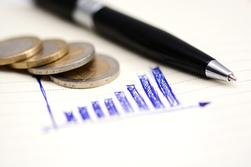 Ascending bar graph on notebook with coins and office tools 