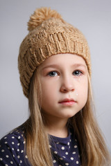 A little cute little girl in a knitted hat on a gray background.