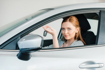 Smiling young woman sitting in new car and holding key