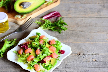 Healthy salad with salmon slices, fresh avocado and lettuce leaves mix on a plate. Fresh avocado half, fork, olive oil jar on vintage wooden background with copy space for text