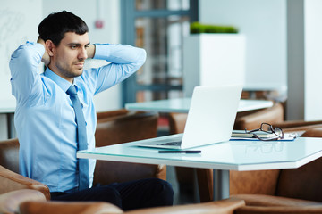 Obraz premium Tired handsome financial manager putting hands on nape and searching mistake in his calculations on laptop, waist-up portrait