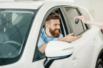 Fototapeta premium Seller giving key to happy young bearded man sitting in new car