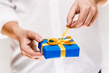 Male hands holding a gift box. Present wrapped with ribbon and bow. Christmas or birthday blue package. Man in white shirt pulls the ribbon.