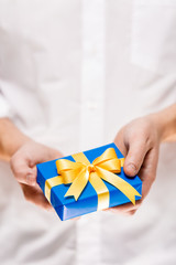 Male hands holding a gift box. Present wrapped with ribbon and bow. Christmas or birthday blue package. Man in white shirt.