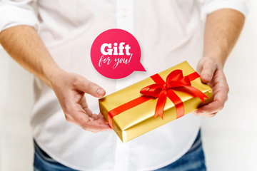 Male hands holding a gift box. Present wrapped with ribbon and bow. Gift for you speech bubble. Man in white shirt.