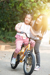 Obraz premium Mother helping daughter learn biking outdoor.