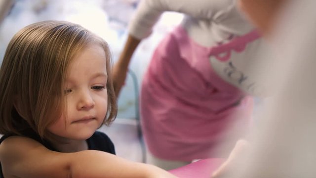 Nail artist doing manicure for pretty little girl in professional salon. Close up view of manicure master applying gel polish