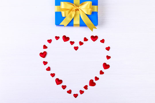 Gift box with red heart. Present wrapped with yellow ribbon. Christmas or birthday blue package. On white wooden table.