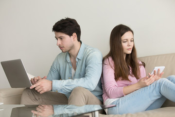 Young couple sitting back to back at home using laptop computer and tablet, internet addiction, online shopping, ignoring and obsessed, not talking to each other, problems in relationships concept