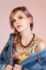 Young girl with colored lock of hair in a colorful dress and denim jacket, isolated on a pink background