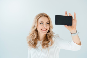 Naklejka premium portrait of smiling woman making selfie on smartphone on grey