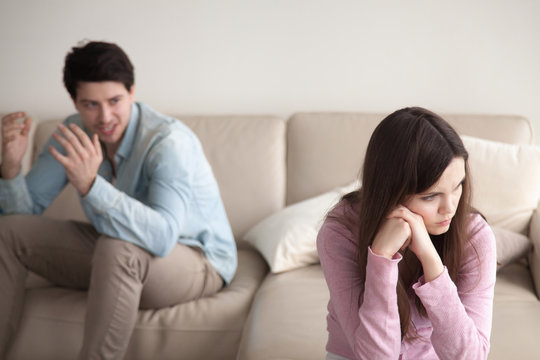 Unhappy couple quarrelling, sitting apart indoors. Aggressive guy is blaming woman, shouting at her. Annoyed girl ignoring man, not talking to boyfriend. Family problems concept, teenagers conflict