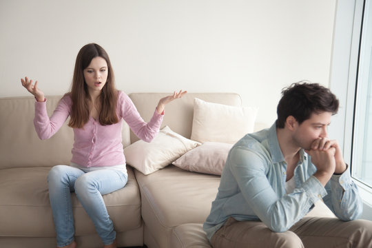 Couple arguing. Young woman speaking emotionally, blaming man, gesturing, explaining opinion. Unhappy girlfriend shouting to frustrated boyfriend, guy sitting back not talking to her. Family quarrel