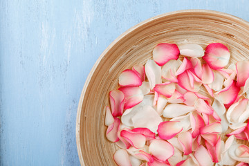 Petals of white and pink roses on blue painted rustic background. Fresh natural flowers in bowl. Dirty grunge wooden board.