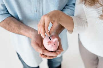 Cropped shot of couple putting coin into small piggy bank