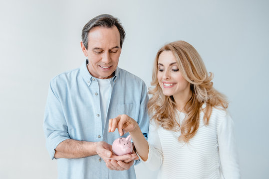 Smiling middle aged couple putting coin into small piggy bank