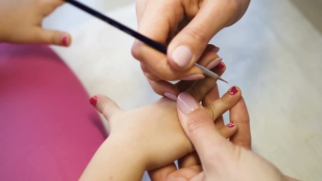 Nail artist doing manicure for little girl in professional salon. Close up view of manicure master applying gel polish and making dots. Hands close up view