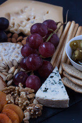 assorted cheese, grapes, crackers, nuts and olive on a black backgtound