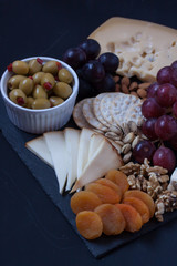 assorted cheese, grapes, crackers, nuts and olive on a black backgtound