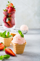 Strawberry ice cream with mint leaves in waffle cups on gray stone background. Homemade summer food concept with copy space.