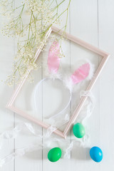 Easter bunny ears in a frame for pictures and colorful eggs on a white background. Top view and space for text