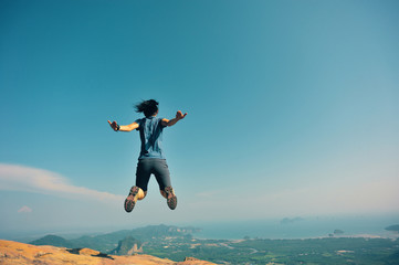 Fototapeta na wymiar successful woman jumping on rocky mountain peak, freedom, risk, challenge, success concept
