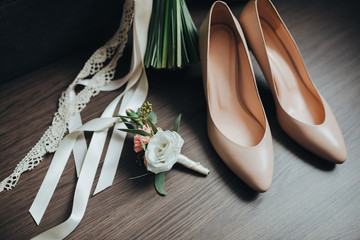 wedding bouquet of flowers and greens with ribbons stands on a wooden floor near the sofa next to the bride's shoes and the groom's buttonhole