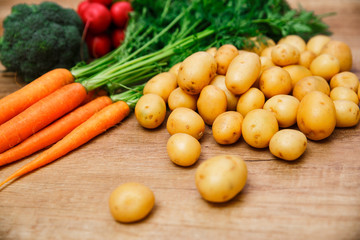 Potatoes with carrot. Red radish, brocoli and raw new potato. Fresh natural vegetables. Organic bio food. On wooden table.