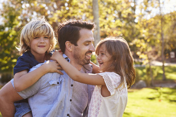 Father Carrying Son And Daughter As They Play In Park